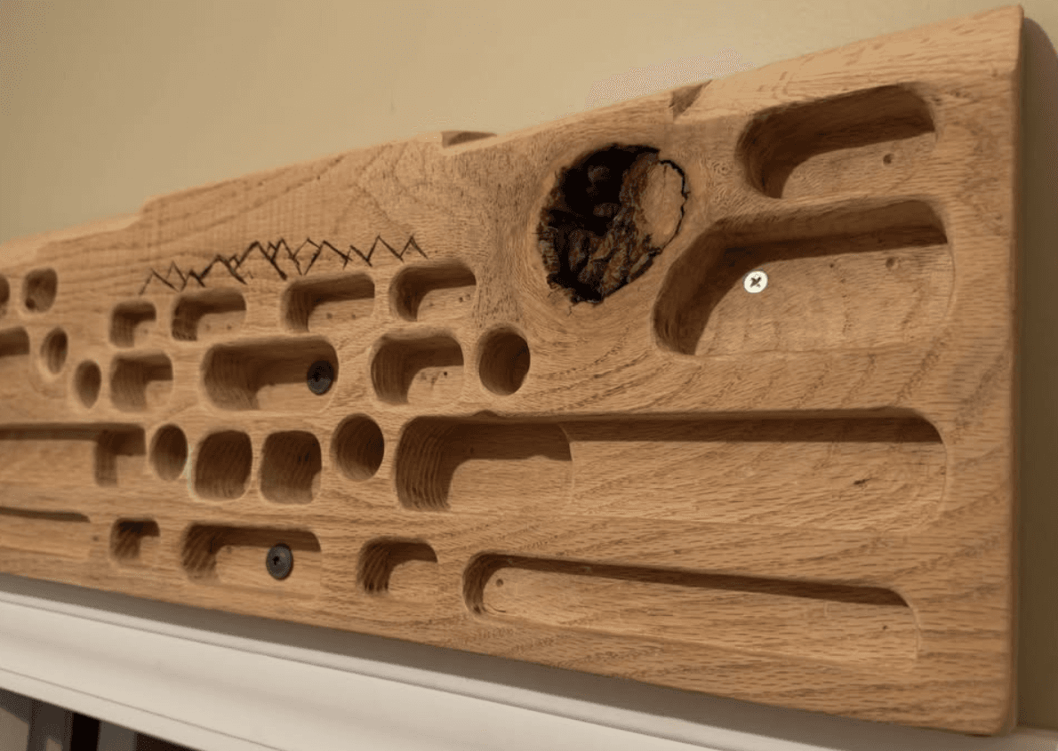 Angled view of the oak hangboard showing the exposed knot and the woodburned mountain detail