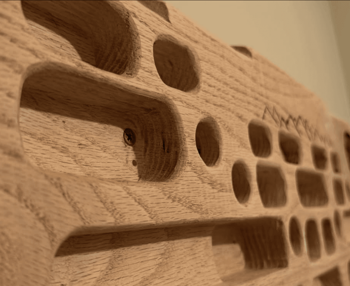 Macro view along the oak hangboard showing the rounded edges and grain of the routed pockets