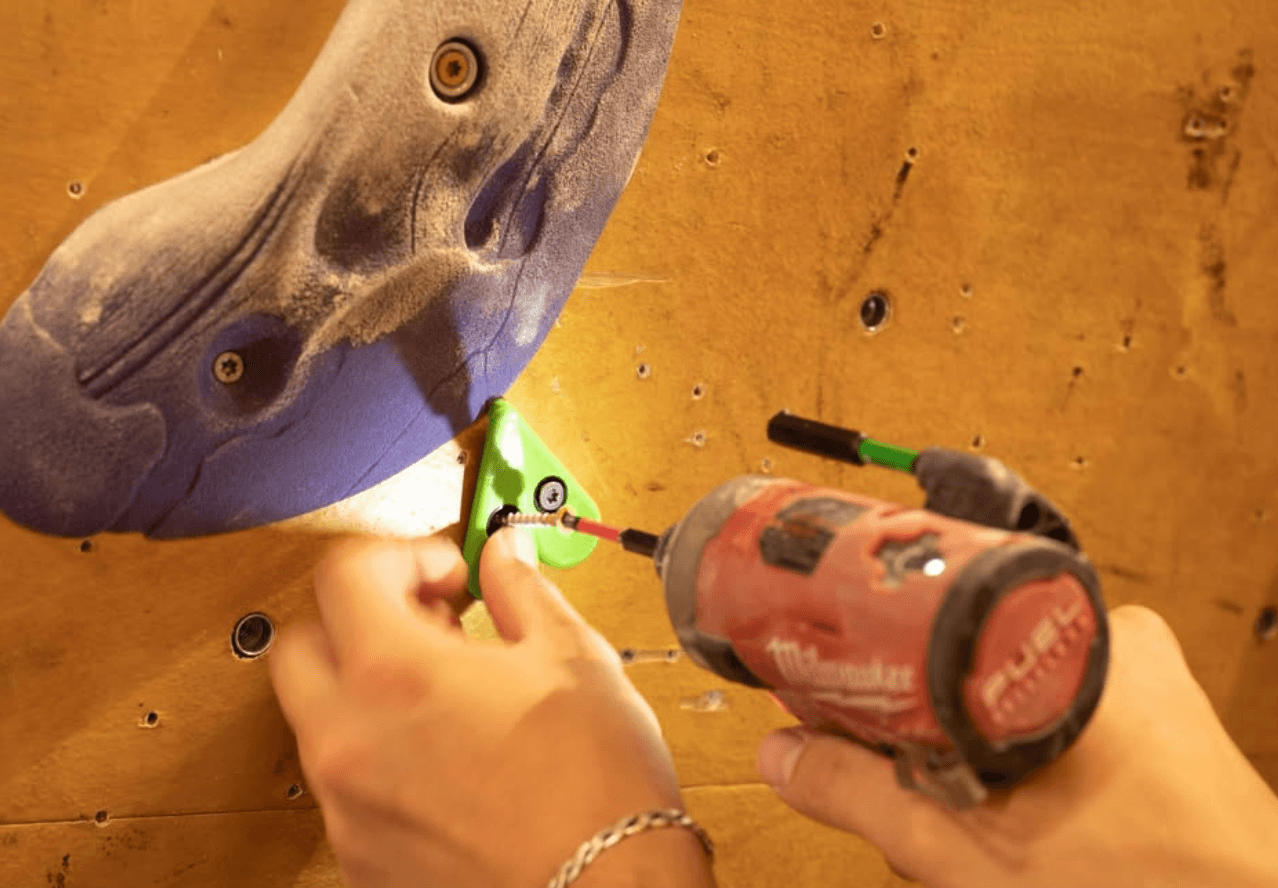 Route tag being installed next to a climbing hold with a drill