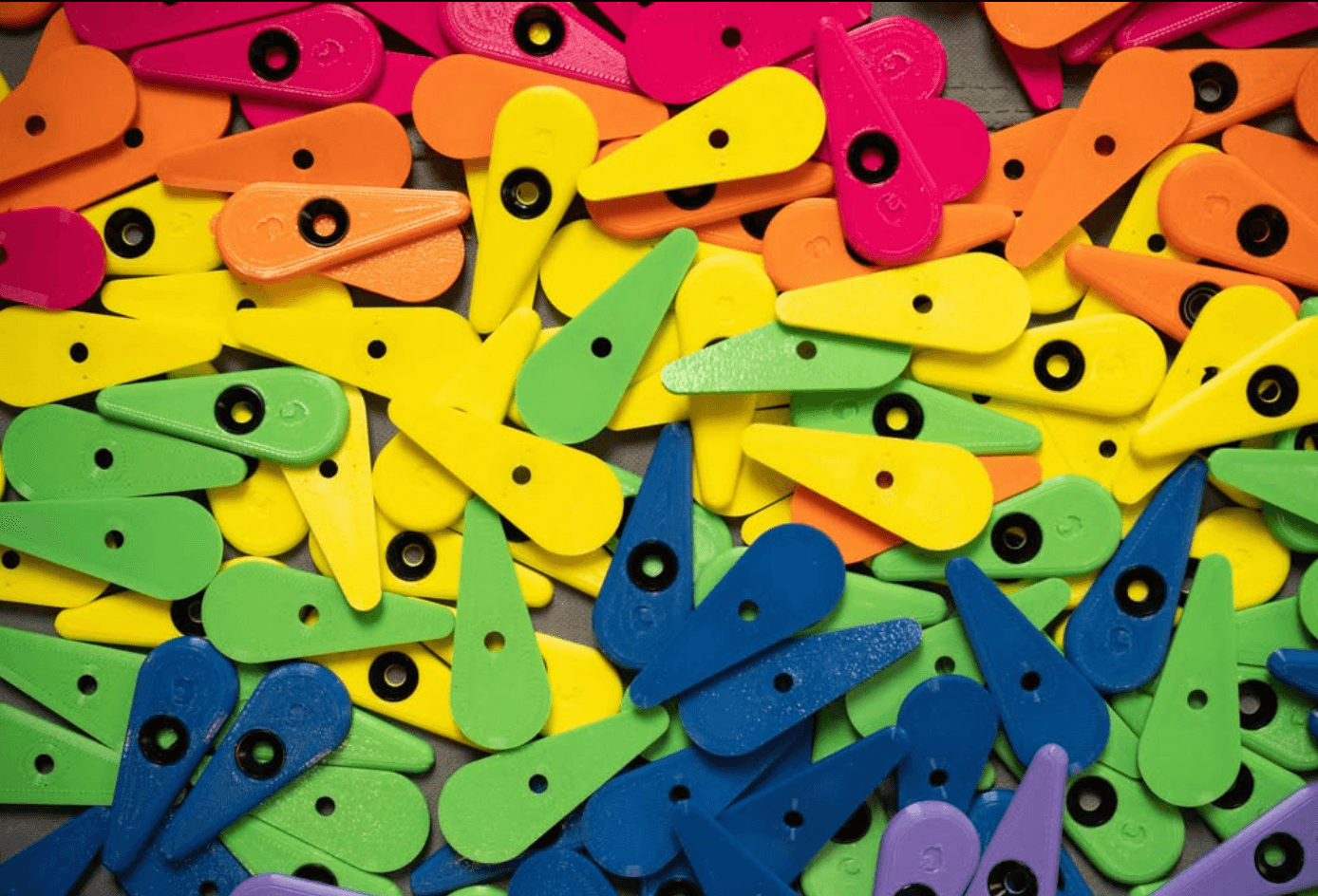 Pile of colorful 3D-printed route tags in pink, orange, yellow, green, blue, and purple