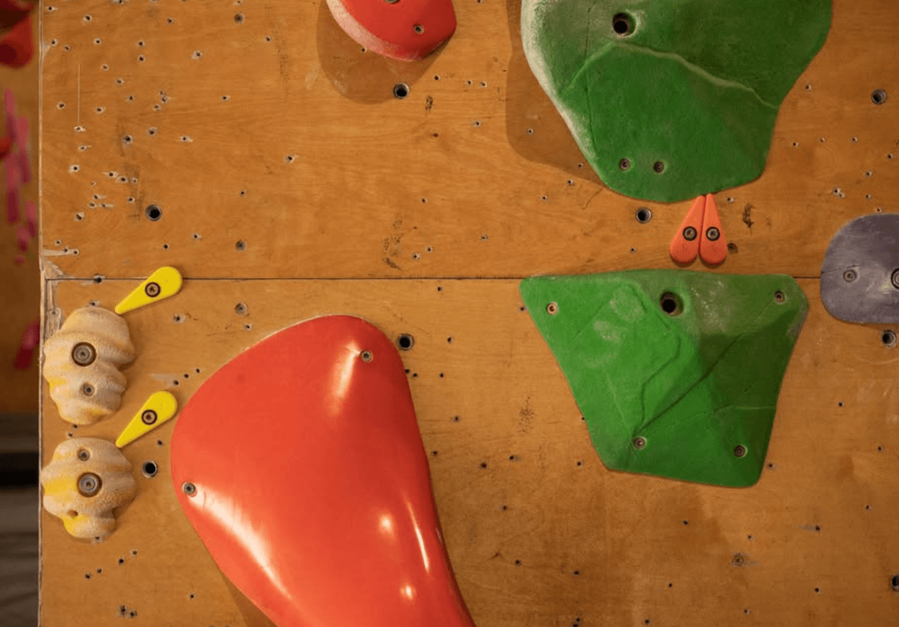 Route tags mounted beside climbing holds on a wooden bouldering wall