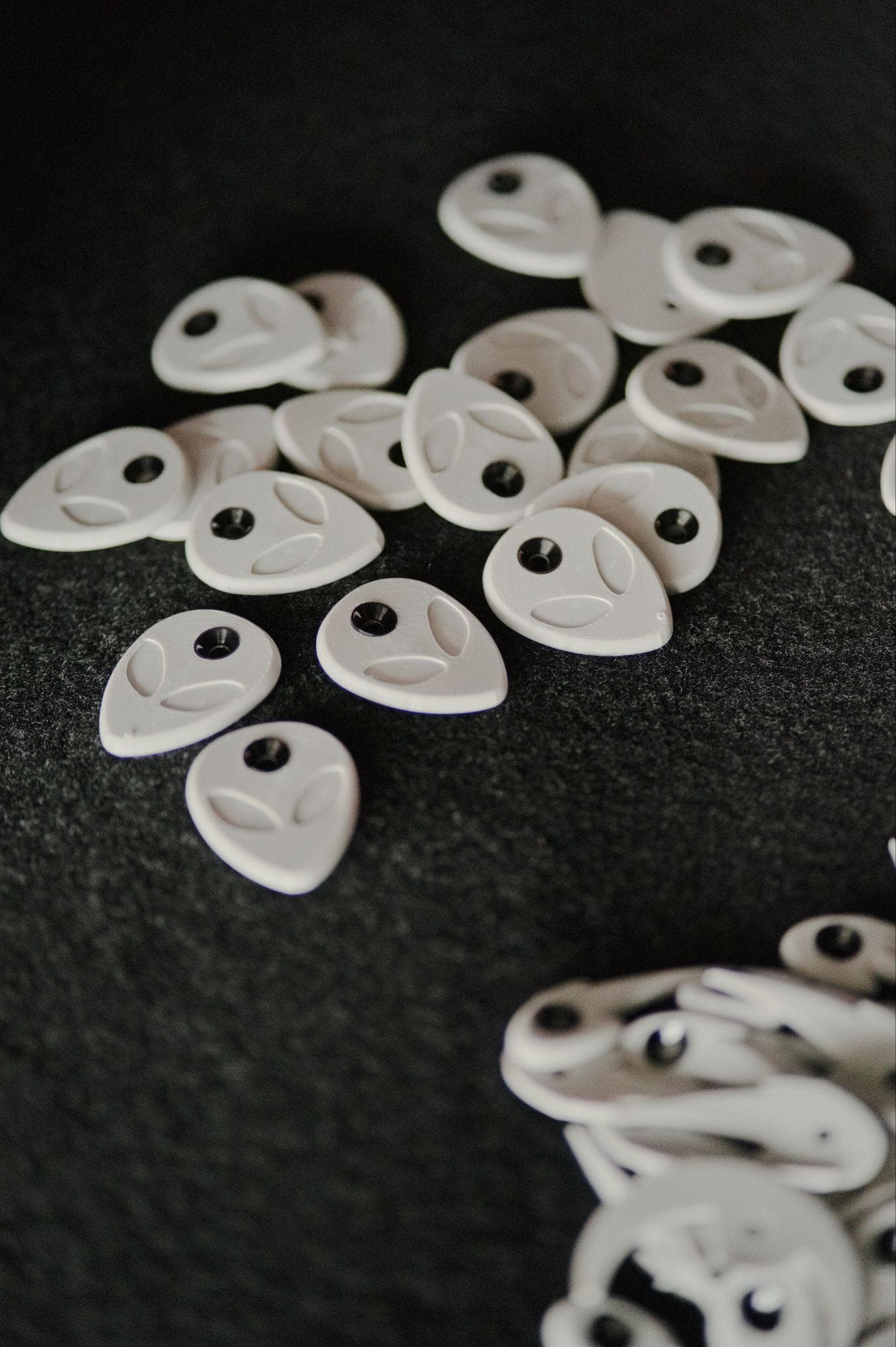 White alien-head route tags laid out on dark felt, each with a single screw hole