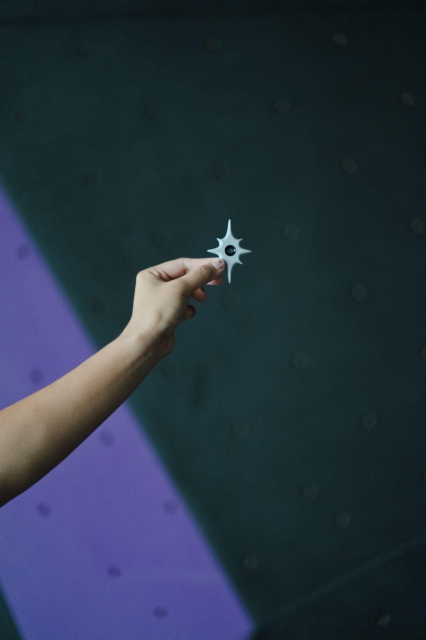 A hand holding a six-point star route tag against a teal climbing wall